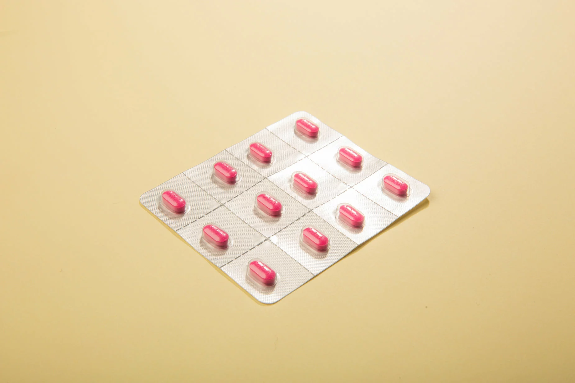 Vitamino B12 supakuotos rožinės tabletės ant dulkėtos geltonos spalvos